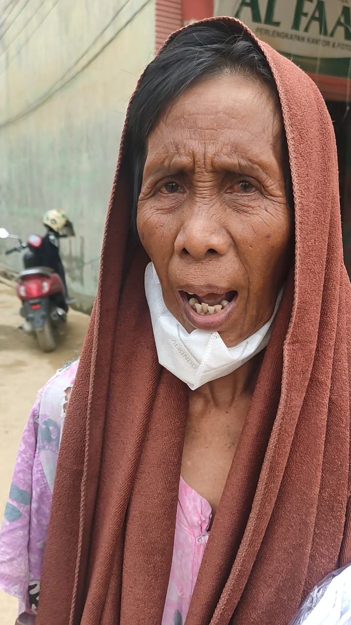 Wak Inem berdiri di tengah reruntuhan rumahnya yang hancur akibat banjir bandang Aceh Tamiang sambil memegang sehelai sarung yang tersisa