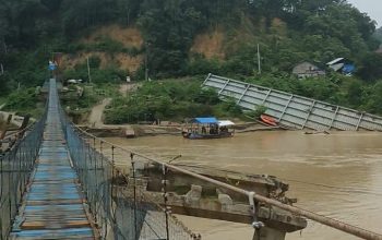 Jembatan gantung berlantai papan biru melintasi Sungai Tamiang, dengan struktur jembatan lain yang tampak rusak di sebelahnya.